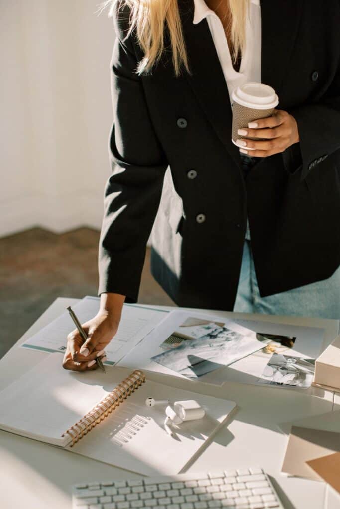 blonde wiman writing in notebook and holding coffee